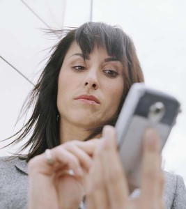 Business woman standing outside in front of office building, using mobile phone